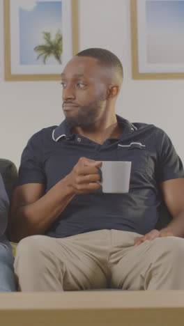 Vertical-Video-Of-Man-Sitting-On-Sofa-At-Home-Looking-At-His-Mobile-Phone-Instead-Of-Talking-To-Friend